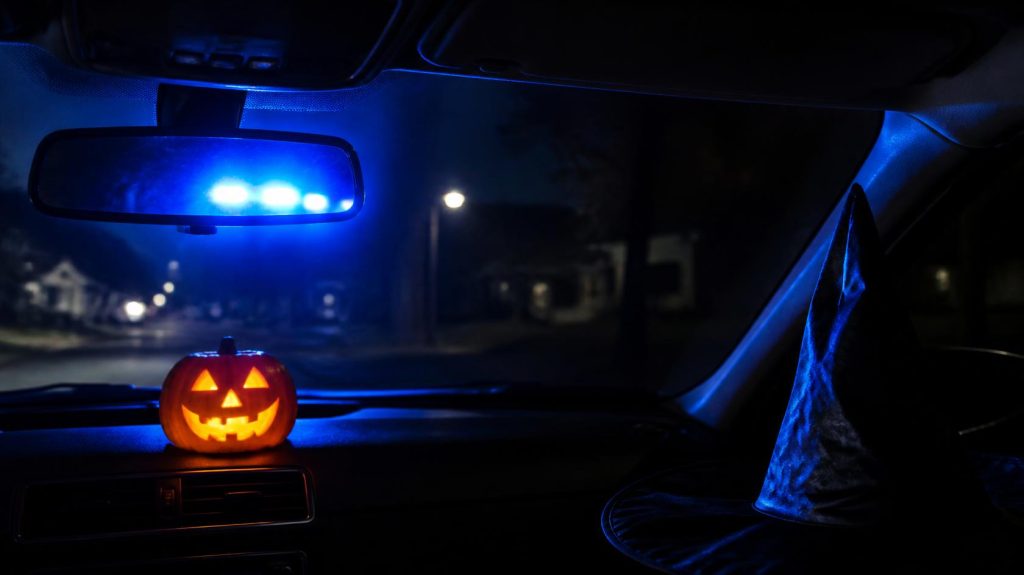 Halloween DUI stop in Florida with police blue lights in the rearview mirror and a jack-o'-lantern on the dashboard